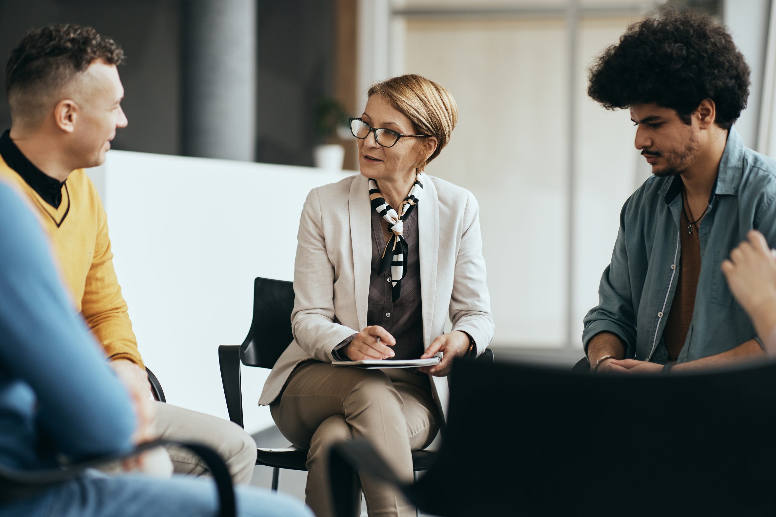 Mature therapist talking to participants of group therapy at mental health center.