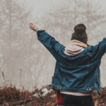 woman in nature in cold weather, back to camera, arms outstretched, celebrating her recovery