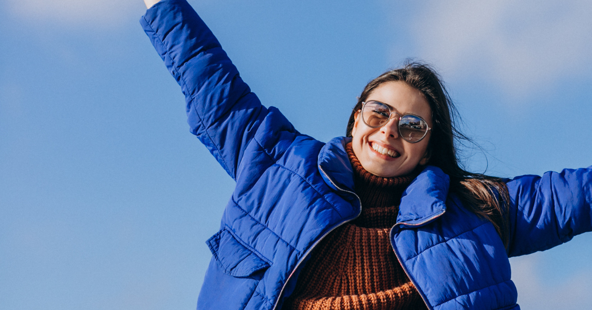 Woman in blue coat and sunglasses, arms wide, ready to start her February recovery journey.