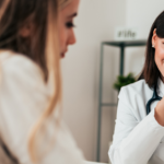 A brunette, woman doctor and a blonde, woman patient discuss a MAT treatment plan in a doctor's office.
