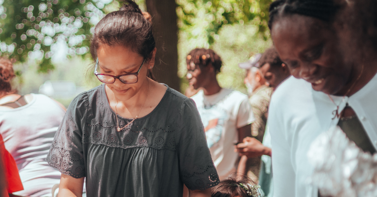 Two women stand in a line to get food at a summer, community gathering — one of the things you can do to practice self care this season.