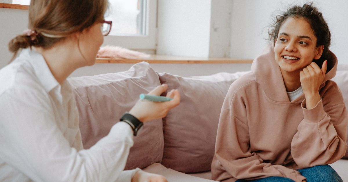 A young woman in recover in a dusty rose pink hoodie speaks with a counselor in a trauma-informed therapy session.